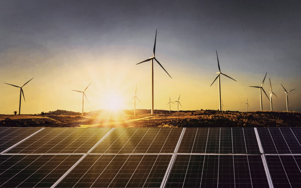 A view of the solar panels with wind turbines in the background